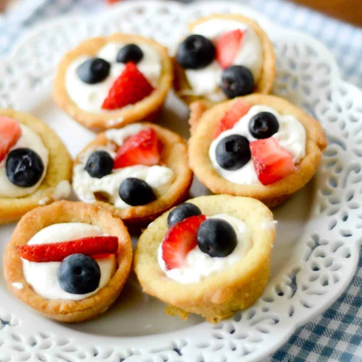 Mini fruit pizza cups topped with strawberries and blueberies.