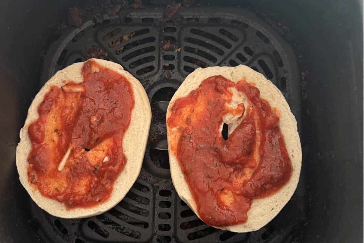 Pizza sauce on white bagels in an air fryer.