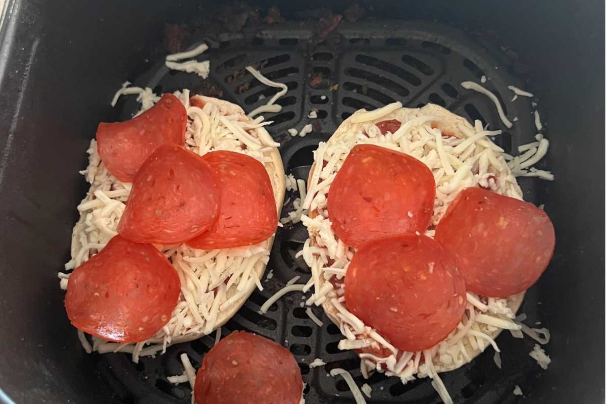 Pizza toppings on white bagels in an air fryer.