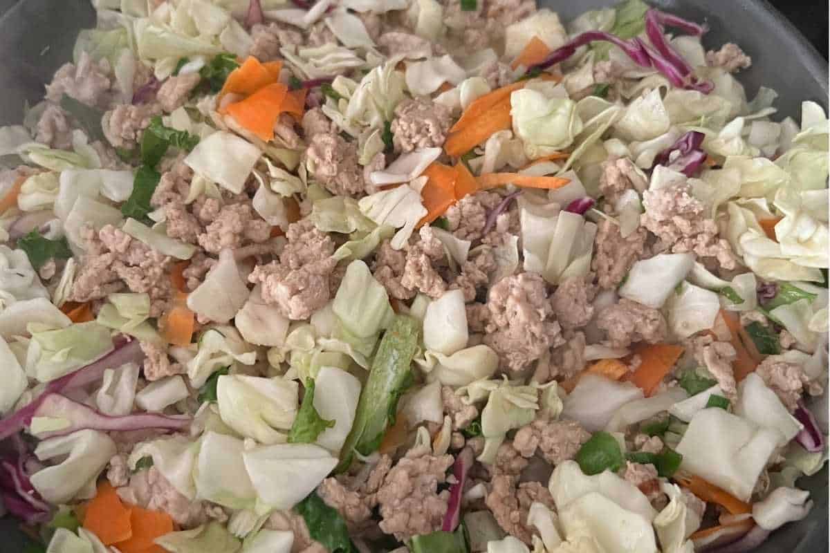 Cooked ground chicken and cole slaw mix cooking in a skillet.