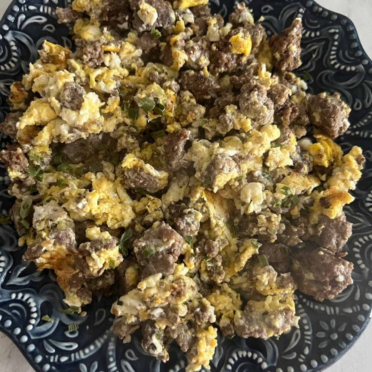 Scrambled eggs and ground beef in a pan on a blue plate topped with chives.