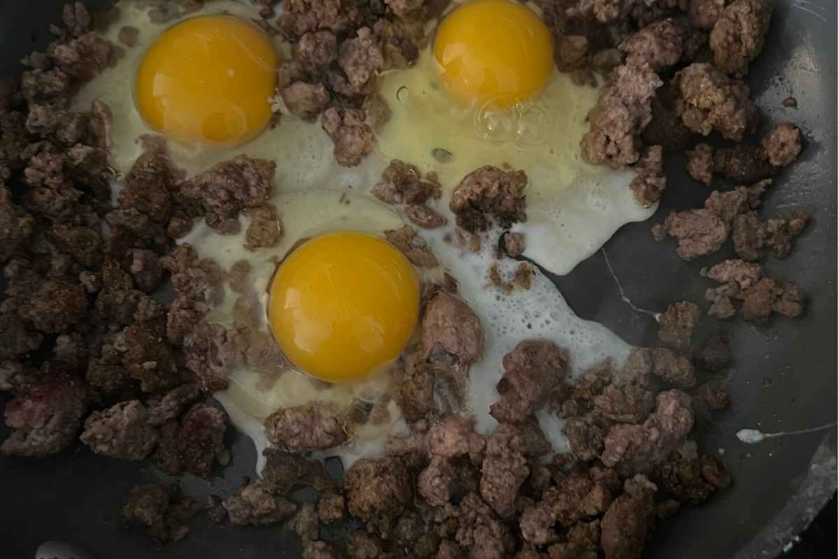 Cracked eggs on top of ground beef in a skillet.