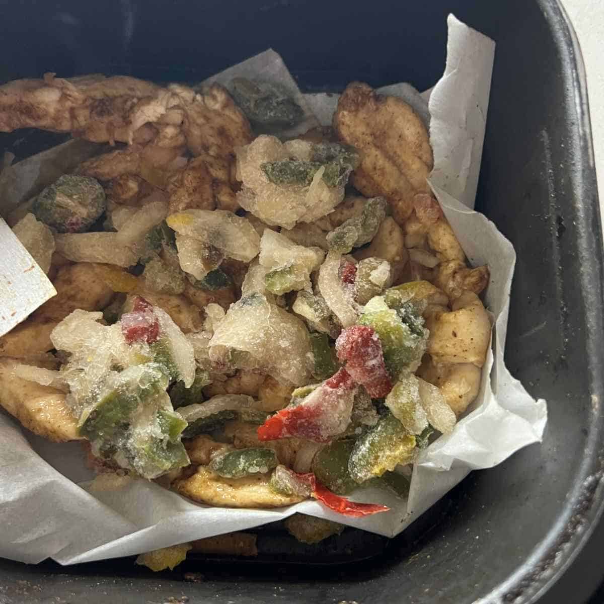 Frozen vegetables and fajita chicken in an air fryer basket. 