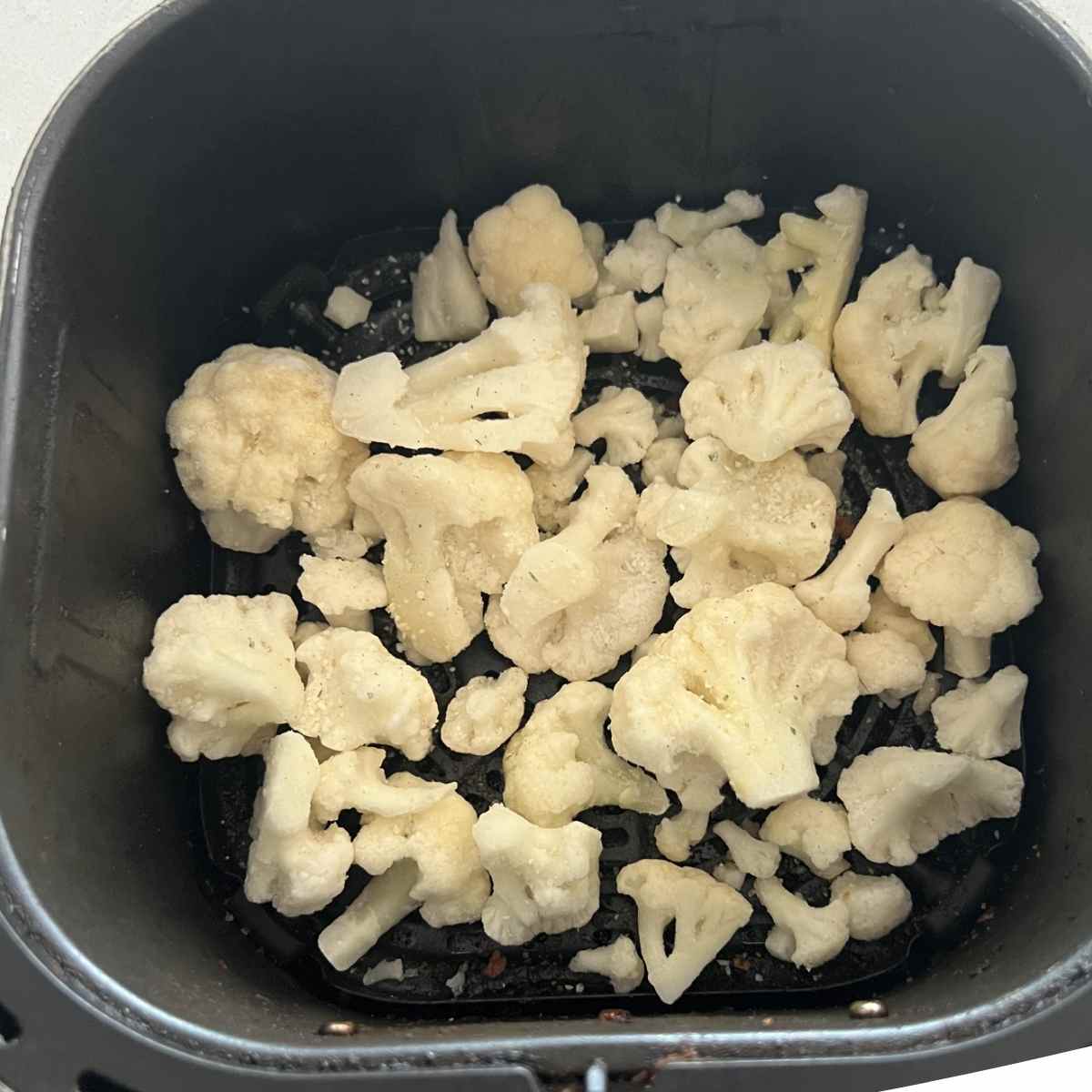 Frozen cauliflower in air fryer basket.