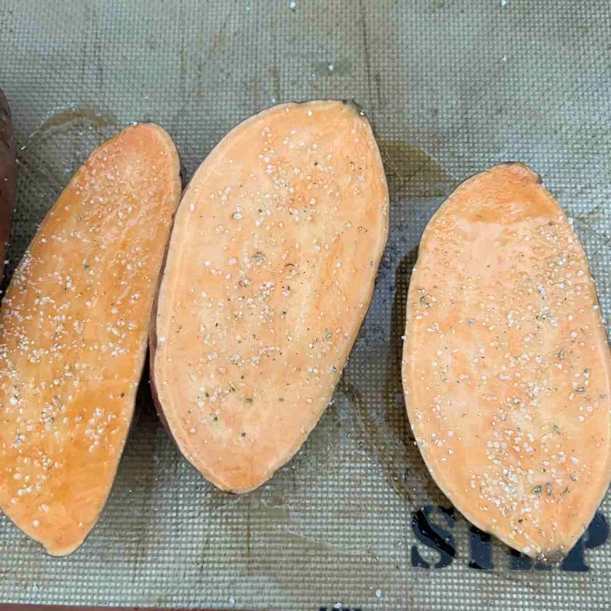 Seasoned sweet potatoes cut in half with maple syrup and olive oil.