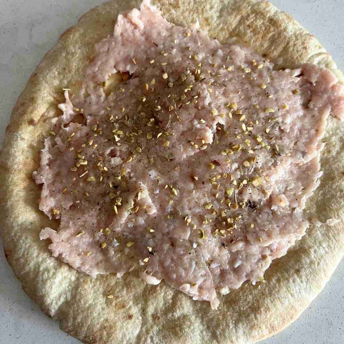 Ground chicken spread on a pita bread. 