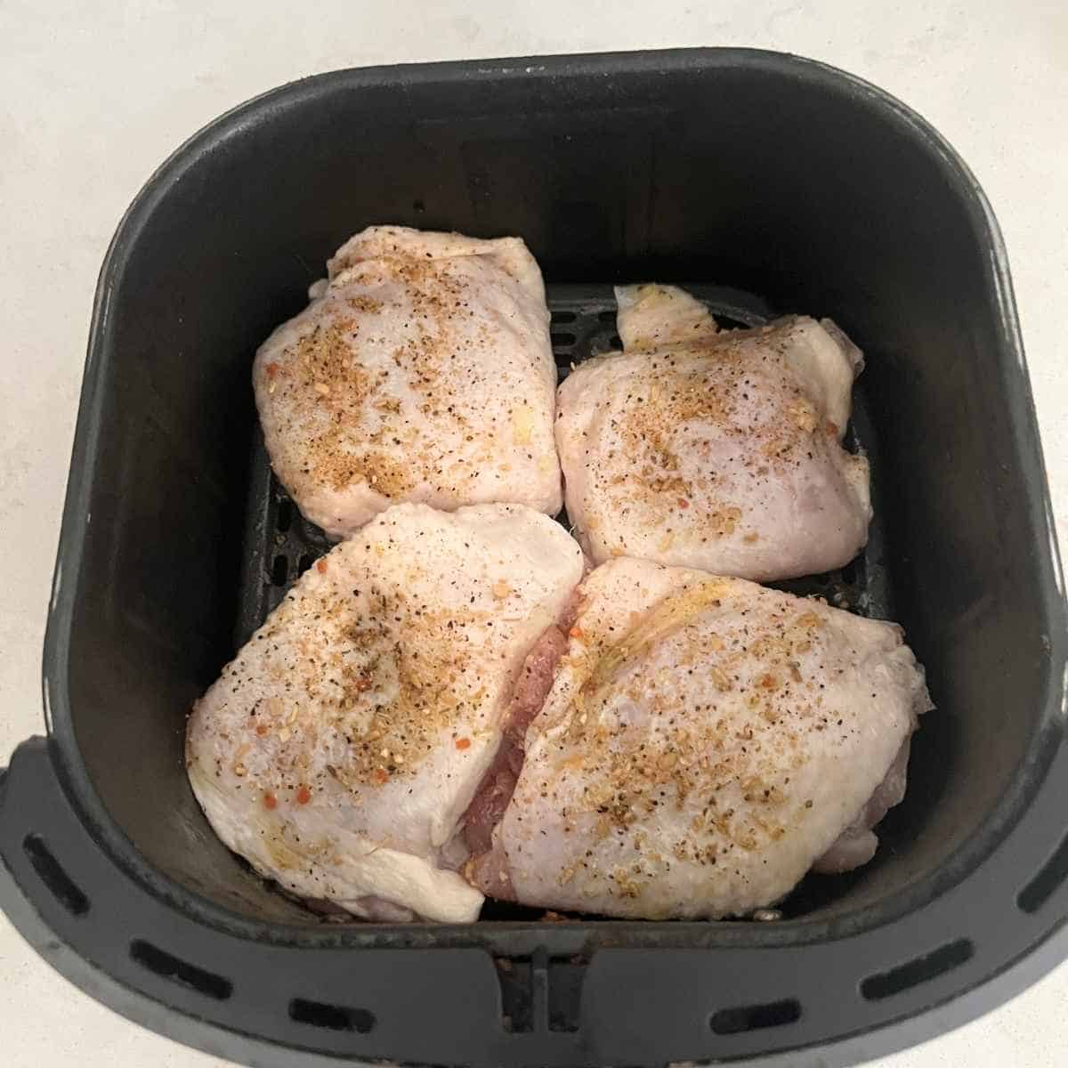 Seasoned chicken thighs in air fryer basket.