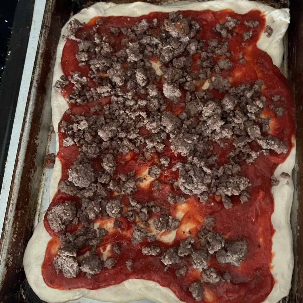 Pizza topped with sauce and ground beef.
