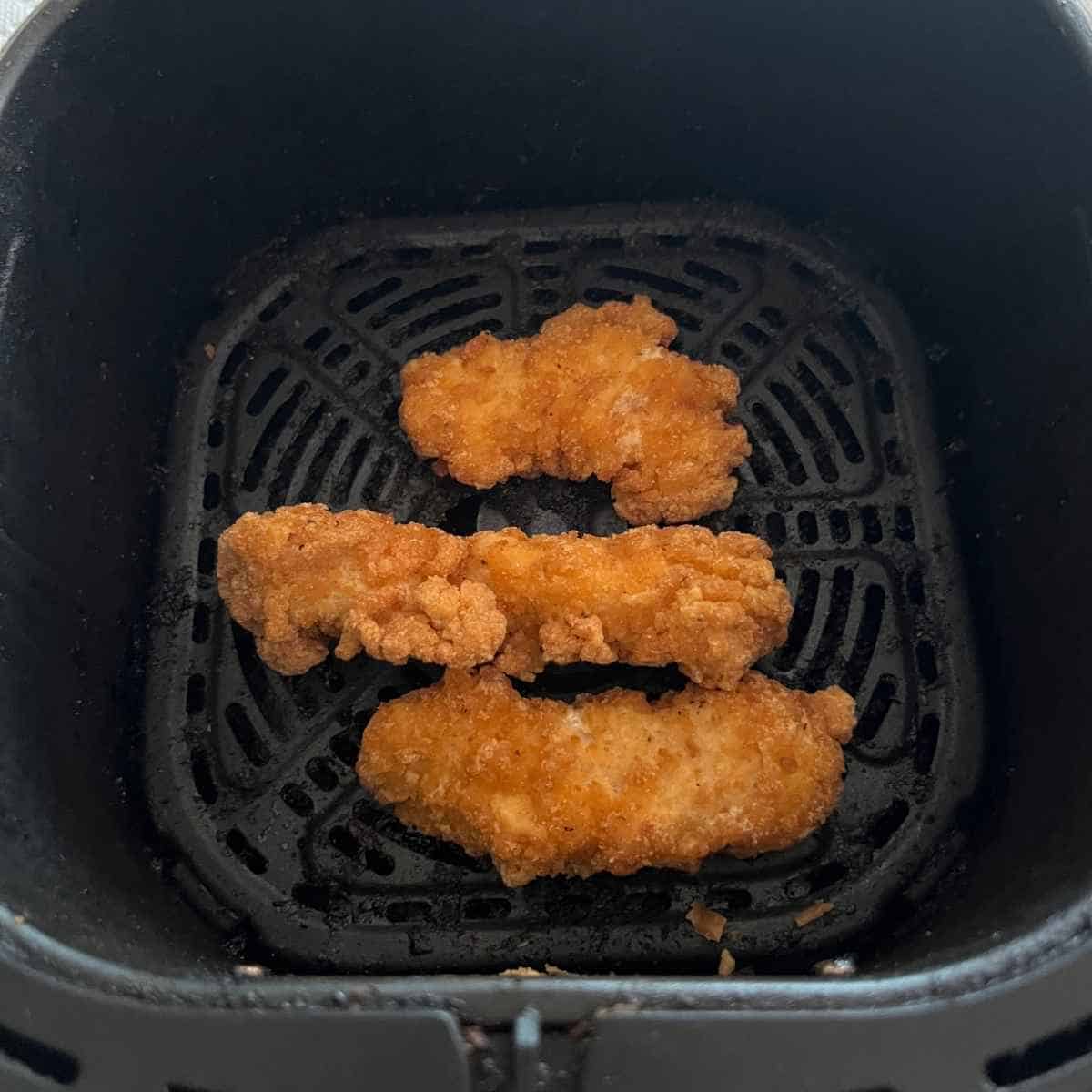 Frozen chicken strips in air fryer basket. 