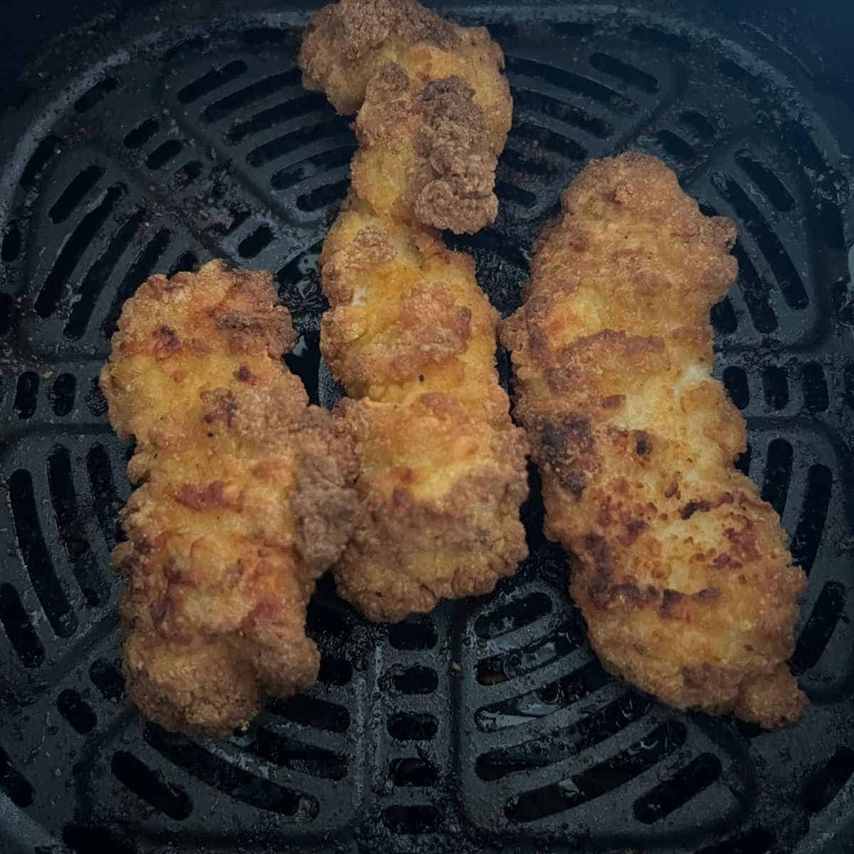 Cooked chicken strips in air fryer basket. 