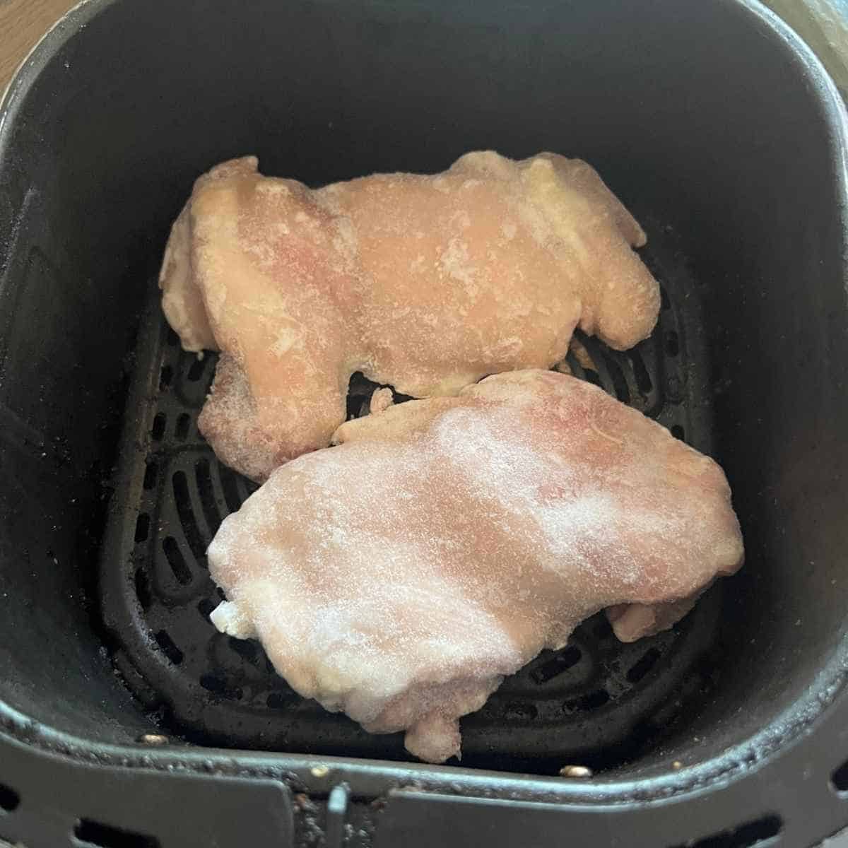 Frozen chicken thighs in air fryer basket.