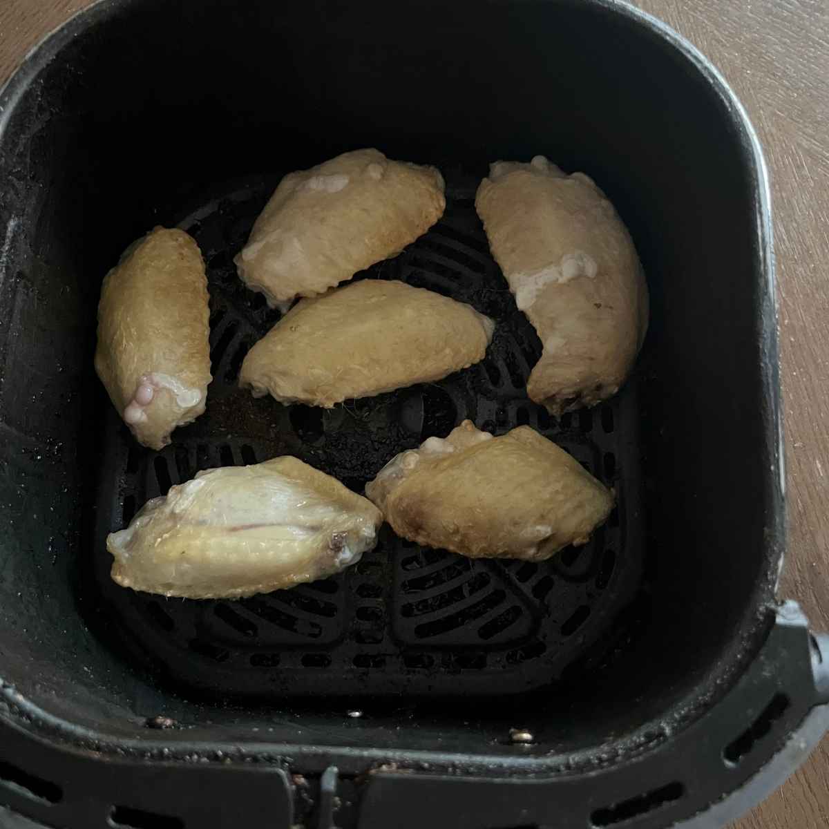Air fryer frozen chicken wings in air fryer basket.