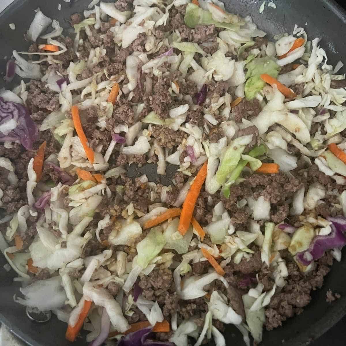 Coleslaw and and ground beef frying in a pan.